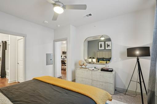 A bedroom with a bed, dresser, mirror, and a ceiling fan.
