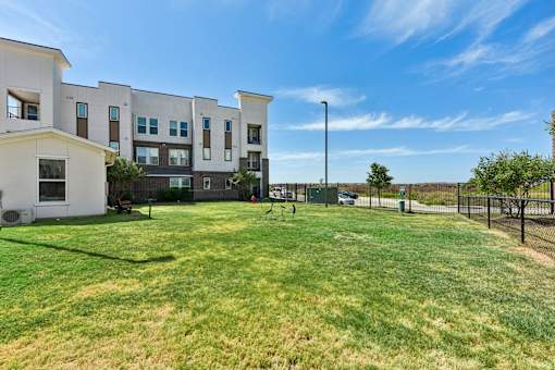 A grassy area in front of apartment buildings with a tennis court and a basketball court.
