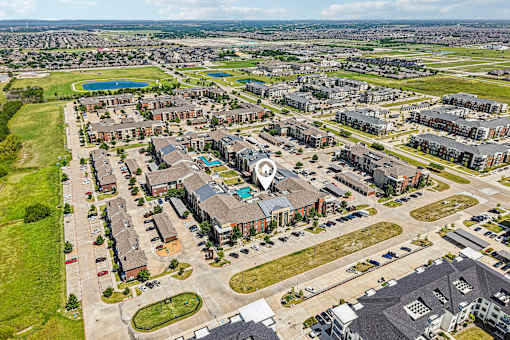 A bird's eye view of a residential area with apartment buildings and a large open space with a pool.