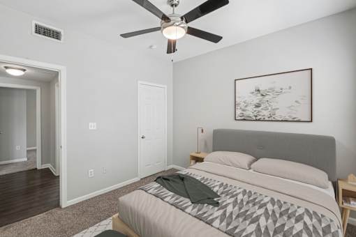 A bedroom with a bed, a ceiling fan, and a painting on the wall.