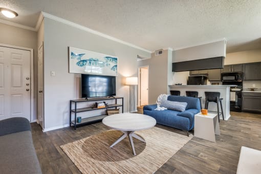 a living room with a couch and a coffee table and a kitchen in the background