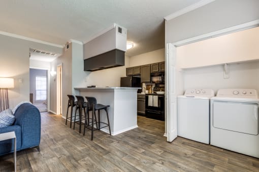 an open kitchen and living room with a washer and dryer and a bar