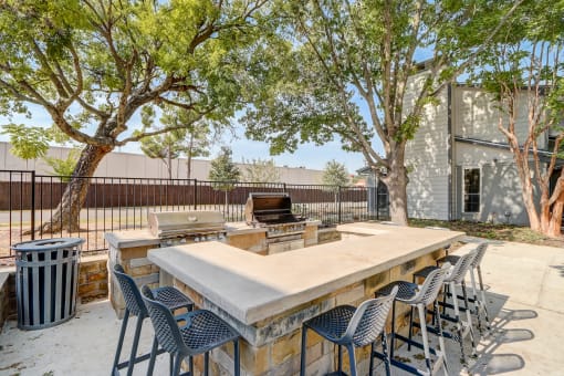 an outdoor patio with a large stone table and chairs and a bbq grill