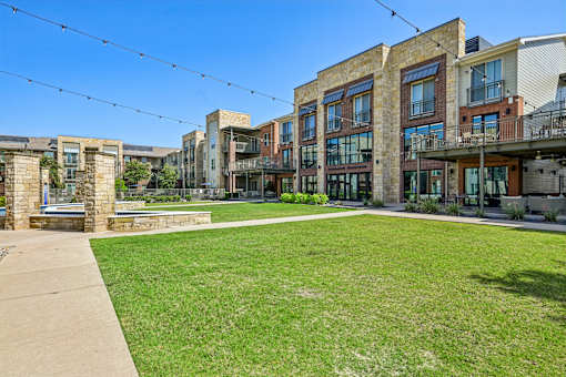 A sunny day in a courtyard surrounded by buildings with a green lawn.