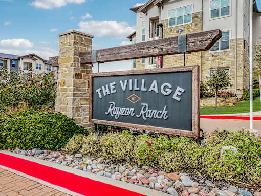 A sign that says "The Village Rayzor Ranch" in front of a building.