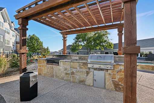 A wooden pergola is over a stone wall with a grill underneath it.