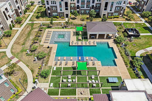 A large swimming pool surrounded by a grassy area and a few buildings in the background.