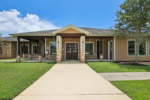 A building with a brown roof and tan walls has a walkway leading to the front door.
