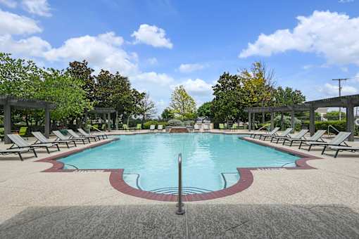 A large pool surrounded by lounge chairs and trees.