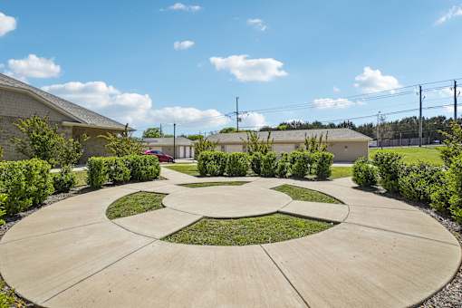 A circular garden with a central island surrounded by bushes and a building in the background.