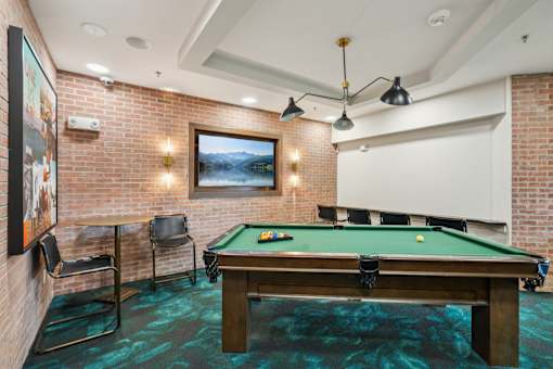 A pool table in a room with a brick wall and a painting hanging on it.