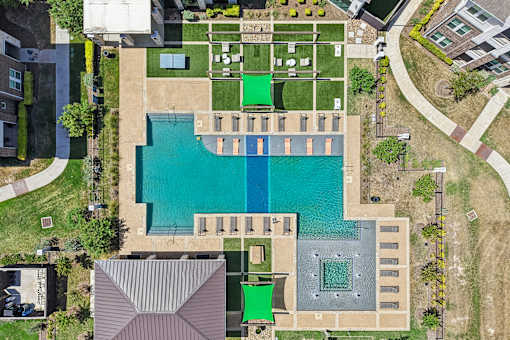 An aerial view of a swimming pool surrounded by a grassy area and buildings.