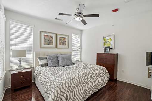 A bedroom with a patterned bedspread, a ceiling fan, and a nightstand with a lamp.