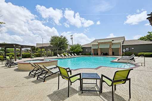 A pool with chairs around it and a building in the background.