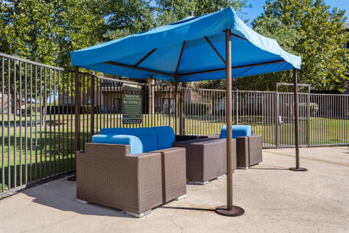 a blue umbrella and three couches in front of a fence