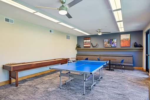 A ping pong table is in the middle of a room with a bench and a fan.