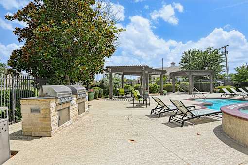 A pool area with a grill and lounge chairs.
