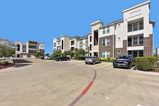 A parking lot in front of apartment buildings with cars parked.