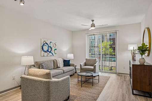 A living room with a grey couch, a chair, a table, and a painting on the wall.