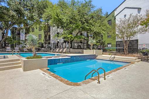 A small pool with a metal ladder is surrounded by a concrete patio and a fence.