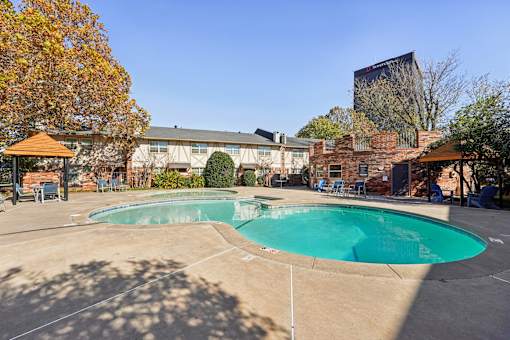 A large outdoor swimming pool surrounded by a patio area with chairs and a gazebo.