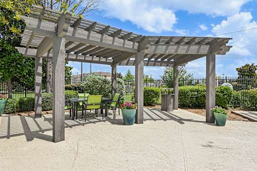 A pergola with chairs and potted plants.