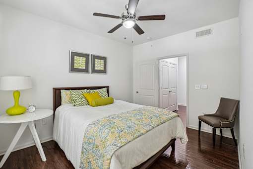 A bedroom with a bed, chair, and ceiling fan.