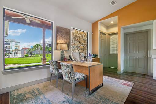 A room with a desk and chairs with a window overlooking a green lawn.