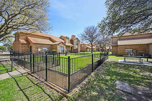 A black fence surrounds a green lawn in front of a brick building.