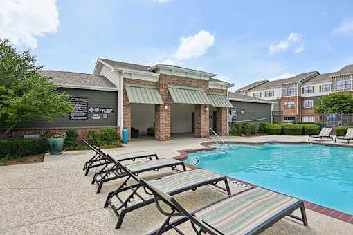 A pool area with sun loungers and a building in the background.