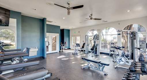 A spacious gym with a variety of equipment and a person working out in the background.