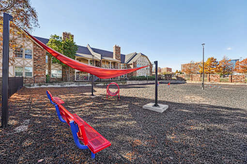 A playground with a red hammock and blue benches.