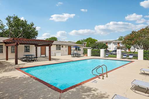 A pool with a red border and a sun shade over a table.