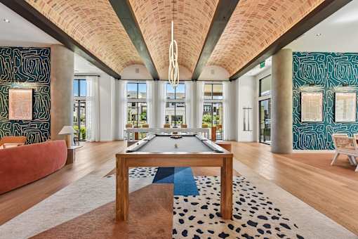 A billiard table in the middle of a room with a wooden floor and a black and white rug.