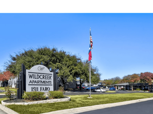 A sign for Wildcreek Apartments stands in front of a parking lot.