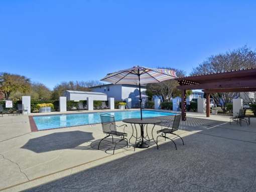 A pool area with a table and chairs under an umbrella.