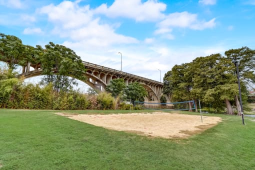 a volleyball court in a park with a bridge in the background