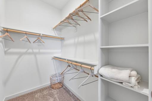 A white closet with clothes hanging and towels on shelves.