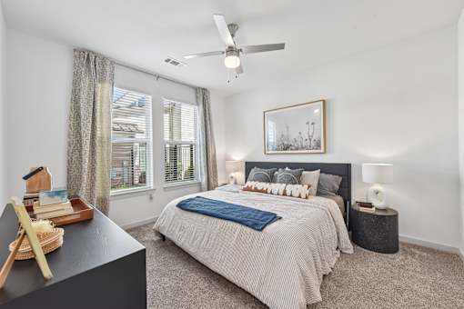 A bedroom with a bed, a fan, and a window with curtains.