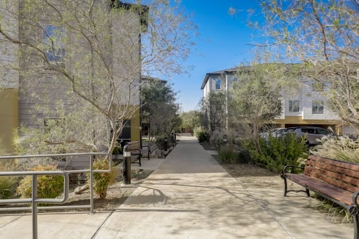 a sidewalk with benches and trees in front of buildings