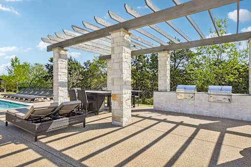 A poolside area with a pergola and lounge chairs.