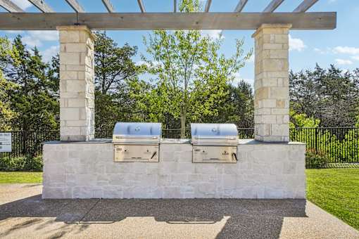 A stone structure with two grills under a wooden pergola.