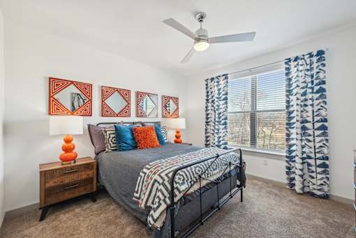 A bedroom with a bed, a ceiling fan, and a window with curtains.
