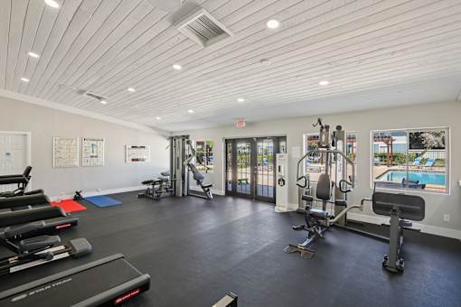 A spacious gym with a variety of equipment and a view of the pool outside.