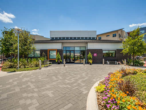 A modern building with a grey facade and a colorful flower bed in front.