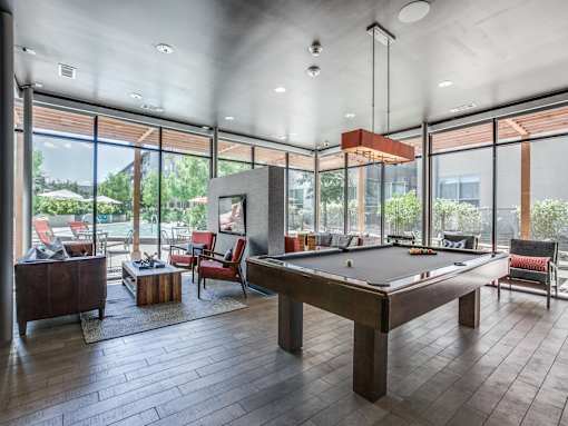 A billiard table is in the middle of a room with a high ceiling and lots of windows.