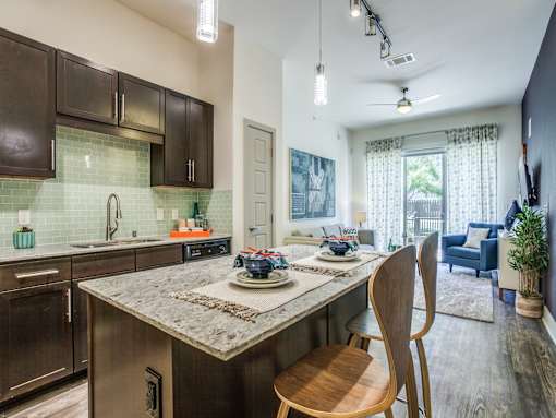 A kitchen with a marble countertop and wooden chairs.