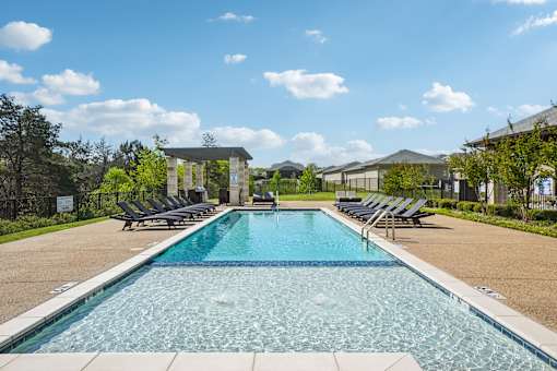 A large swimming pool with lounge chairs and a building in the background.