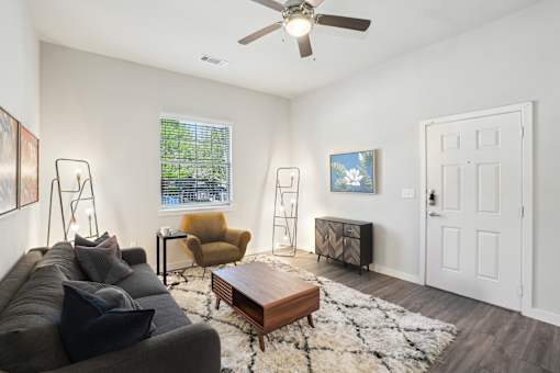 A living room with a grey couch, a yellow chair, a wooden coffee table, and a white rug.
