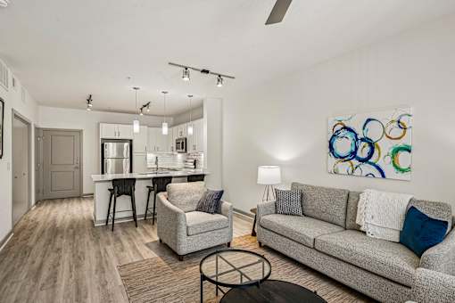 A modern living room with a grey couch, a white coffee table, and a painting on the wall.